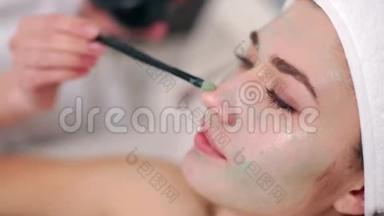 美容专家使用刷子涂抹面膜，使皮肤水润健康。 迷人的女人令人放松